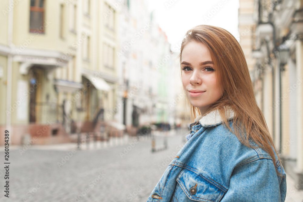 Street portrait of an attractive blonde girl wearing a denim jacket, standing on the street and looking into the camera. Beautiful girl student walking on the street. Street portrait of an attractive blonde girl wearing a denim jacket, standing on the street and looking into the camera. Beautiful girl student walking on the street.