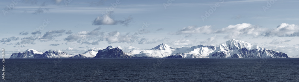 Snow peaks, glaciers and rocks of Aleutian islands in sunny winter day as viewed from ship passing in calm sea
