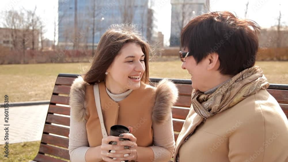 Mother and daughter are sitting in spring Park for coffee break after shopping, happy family and people concept