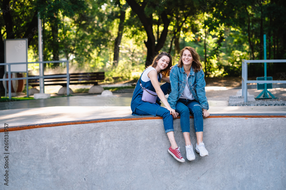 Two happy young girls sitting at the skate park
