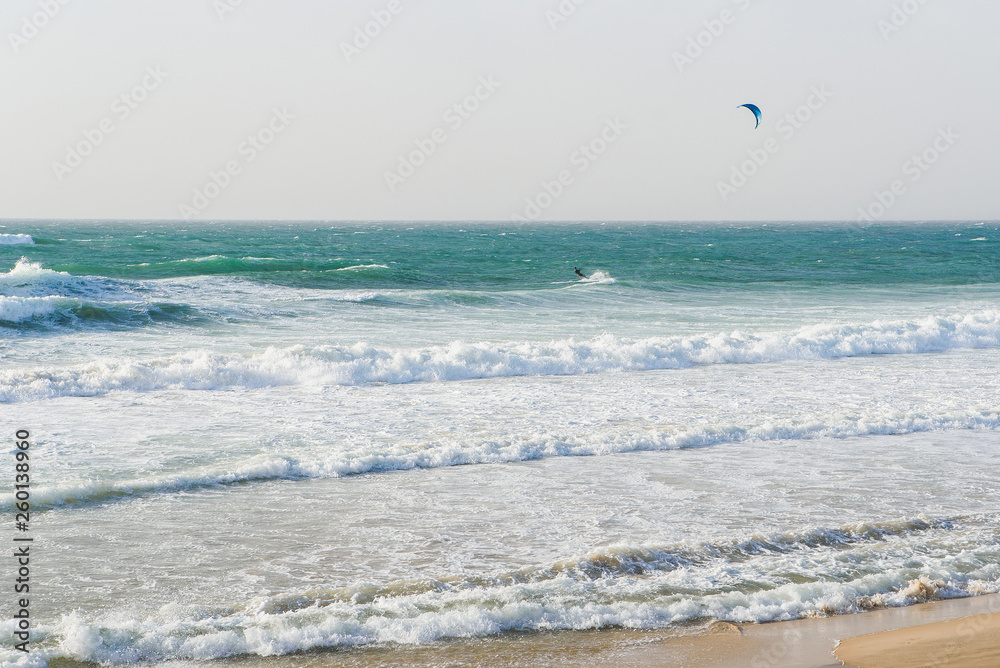 Unrecognisable man with parachute rides on a surfboard on large waves in the sea or ocean.