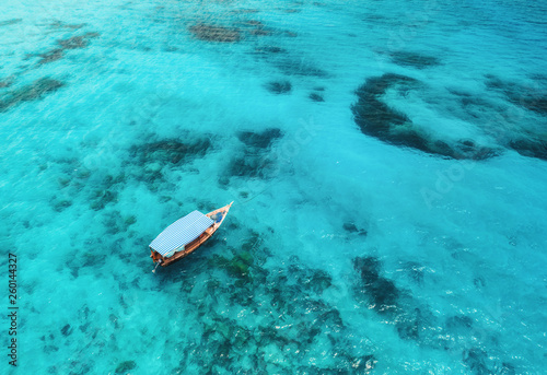 Aerial view of the fishing boat in clear blue water at sunny day in summer. Top view from drone of boat in Indian ocean in Zanzibar, Africa. Landscape with motordboat, transparent sea. Seascape © den-belitsky