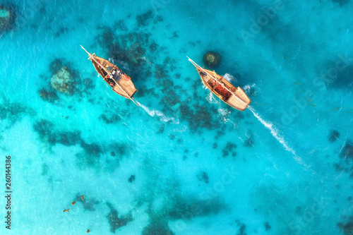 Aerial view of the fishing boats in clear blue water at sunset in summer. Top view from drone of boat, sandy beach. Indian ocean. Travel in Zanzibar, Africa. Landscape with sailboats, sea. Seascape