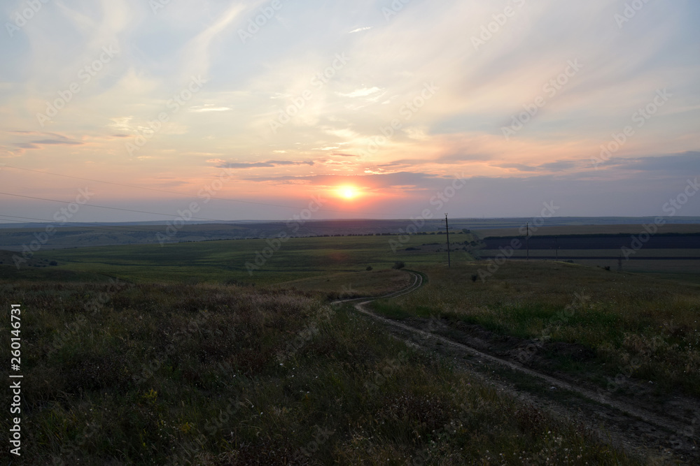 Fototapeta premium Republic of Moldova fields landscape. Countryside sunset with dirty road between fields in Moldova.