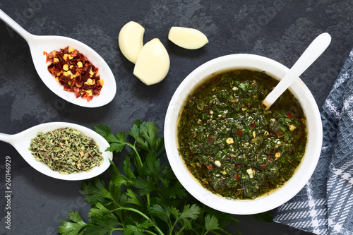 Raw homemade Argentinian green Chimichurri salsa or sauce made of parsley, garlic, oregano, hot pepper, olive oil, vinegar, photographed overhead with natural light (Selective Focus on the salsa) photo