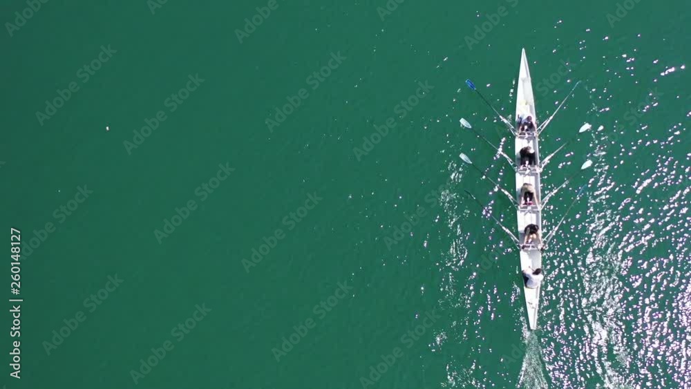 Aerial drone bird's eye top view video of sport canoe operated by team of young men and women in open ocean sea