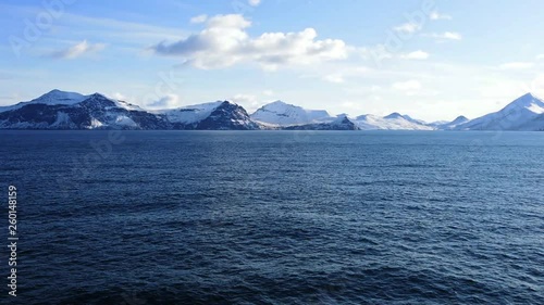 Snow peaks, glaciers and rocks of Aleutian islands in sunny winter day as viewed from ship passing in calm sea photo