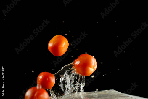 Fresh tomato dropped into water, isolated on dark background