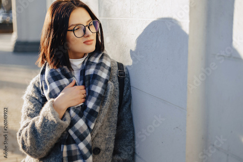 Attractive young girl wearing glasses in a coat walking on a sunny day