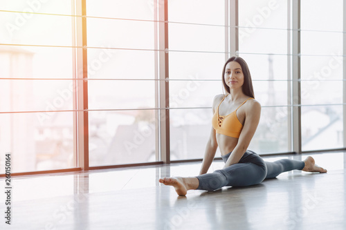 young attractive girl doing fitness exercises with yoga on the floor against the background of panoramic windows