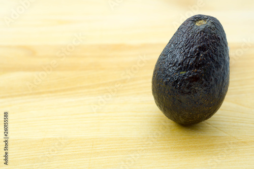 single standing ripe avocado off the side on a light brown wooden table