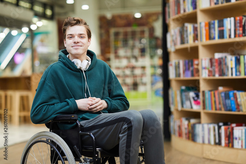 Leinwand Poster Content handsome young disabled student with headphones on neck siting in wheelc