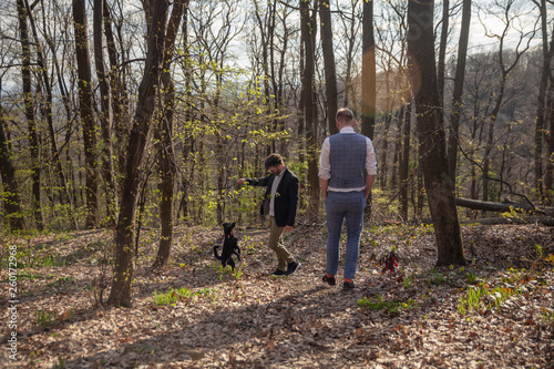 two men, young gay couple walking in forest with their dog.