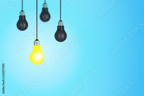 Business Idea Concept : One yellow light bulb of others black light bulb hanging from ceiling with blue background.