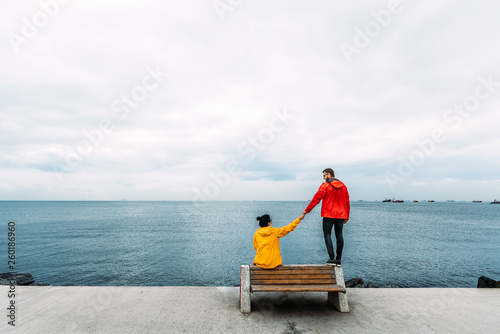 Young couple sitting on a bench by the sea. Man and woman traveling. People sit on a bench and look at the sea. Tourists by the sea. Friends on the bench. A lonely pair. Walking along the promenade