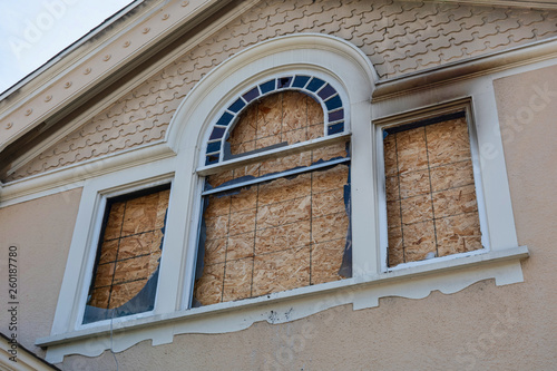 Home window boarded up with plywood sheets. House fire - walls and eves charred.  Plywood shutters prevent unauthorized access by squatters, looters to damaged unused, vacant, or abandoned property.