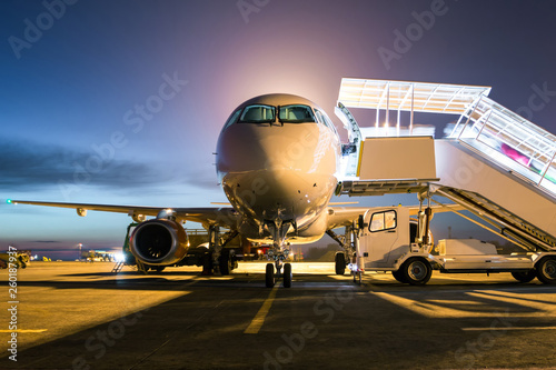 Front view ground handling of white passenger airplane with a boarding steps at the night airport apron