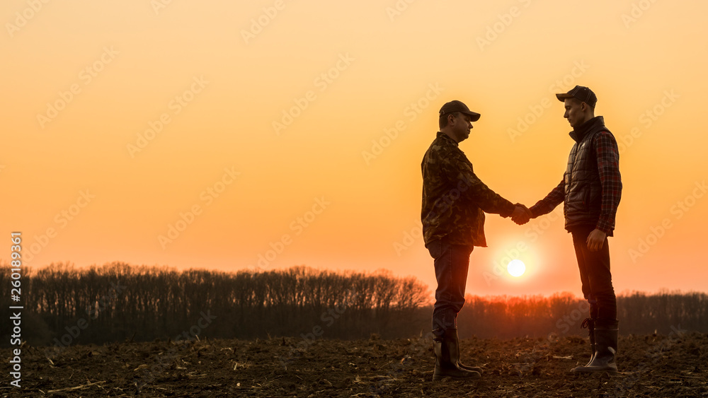 Two farmers on the field shake hands at sunset