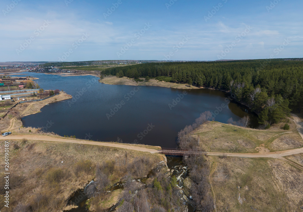 A pond in the Gileva village, a dam, a road bridge and a small waterfall. Sunny, spring, Aerial.