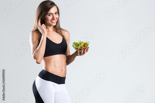 Fit woman in sportswear with a salad on a gray background. © BestForYou