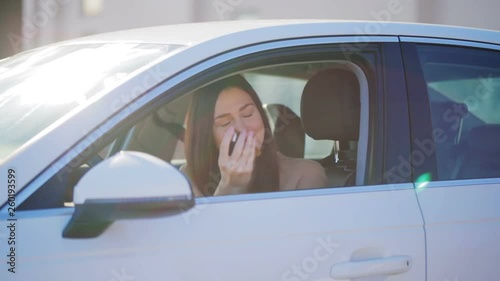 young beautiful woman with long hair in white car takes key with keychain and smiles on sunny day before test drive