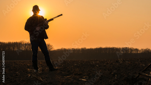 A man with a gun standing in a field at sunset. Opening of the hunting season
