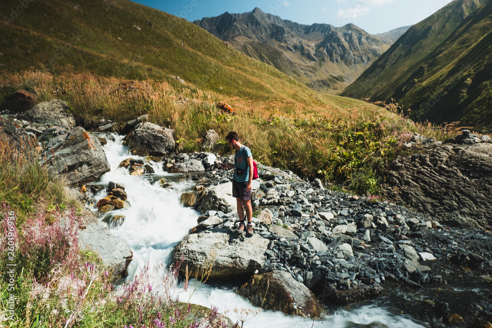 Man standing on rocks in mountain stream water in landscape of Caucasus, Georgia, Asia