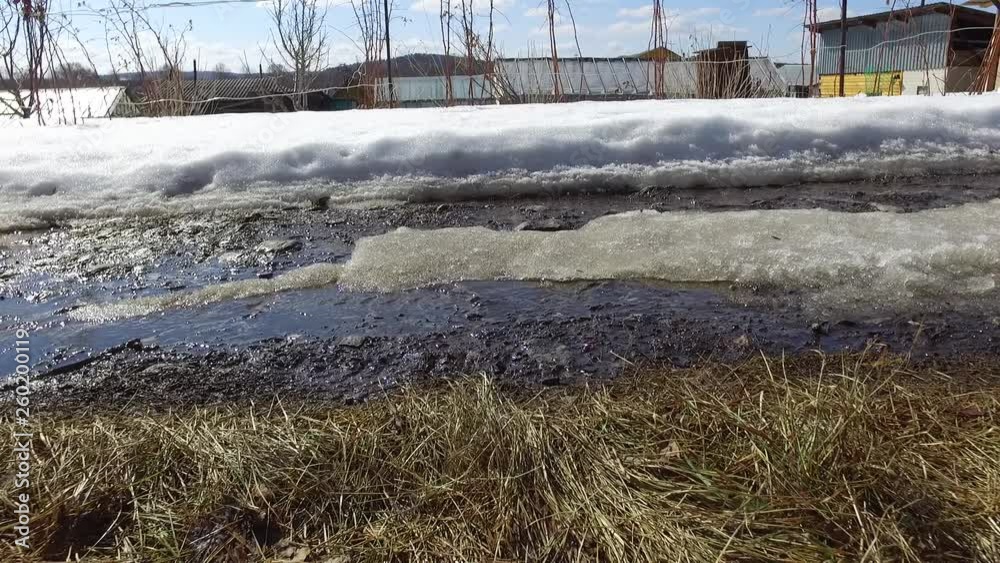 Close-up. Sunny spring day. The snow melts under the sun. Runs stream on the road near the farm. Countryside. Close-up. Sunny spring day. The snow melts under the sun. Runs stream on the road near the farm. Countryside.