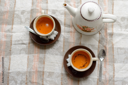 a teapot, two cups of tea on saucers with sugar, tea spoons on a