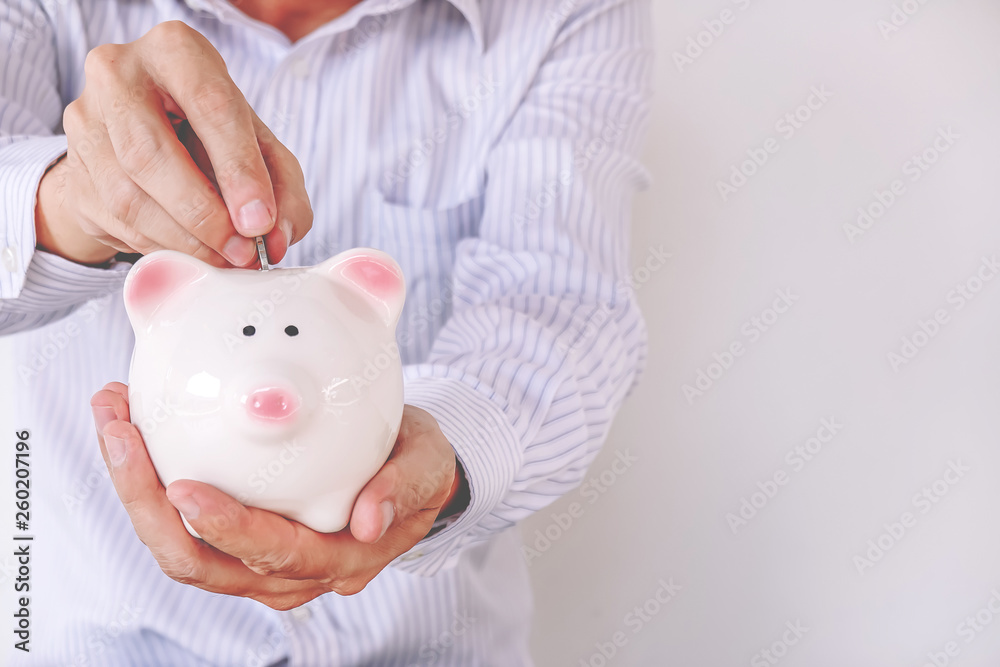 Close-up of a businessman putting a coin into a piggy bank against a white background . Close-up of a businessman putting a coin into a piggy bank against a white background .