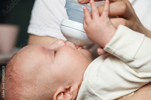 Baby drinking milk from bottle holding by father. Healthy nutrition