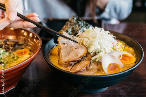 Photography Woman hand pinching noodle in Ramen Pork Bone Soup (Tonkotsu Ramen) with Chashu Pork, Scallion, Sprout, Corn, Dried Seaweed and boiled egg served in black bowl