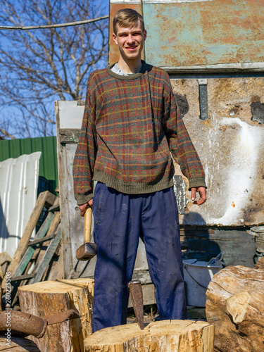 Portrait of a young guy with a wedge and a sledgehammer, harvesting oak firewood photo