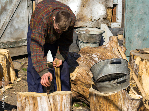 a young guy in the village chopping oak stumps with a wedge and sledgehammer, harvesting wood photo