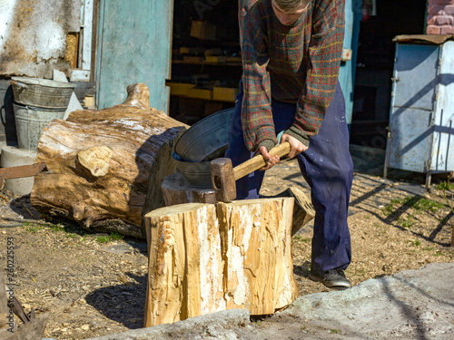 a young guy in the village chopping oak stumps with a wedge and sledgehammer, harvesting wood photo