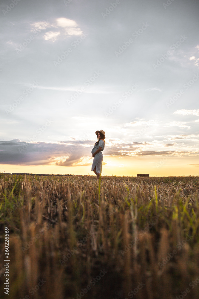 lovely pregnant woman next to the hay bale in the sunlight