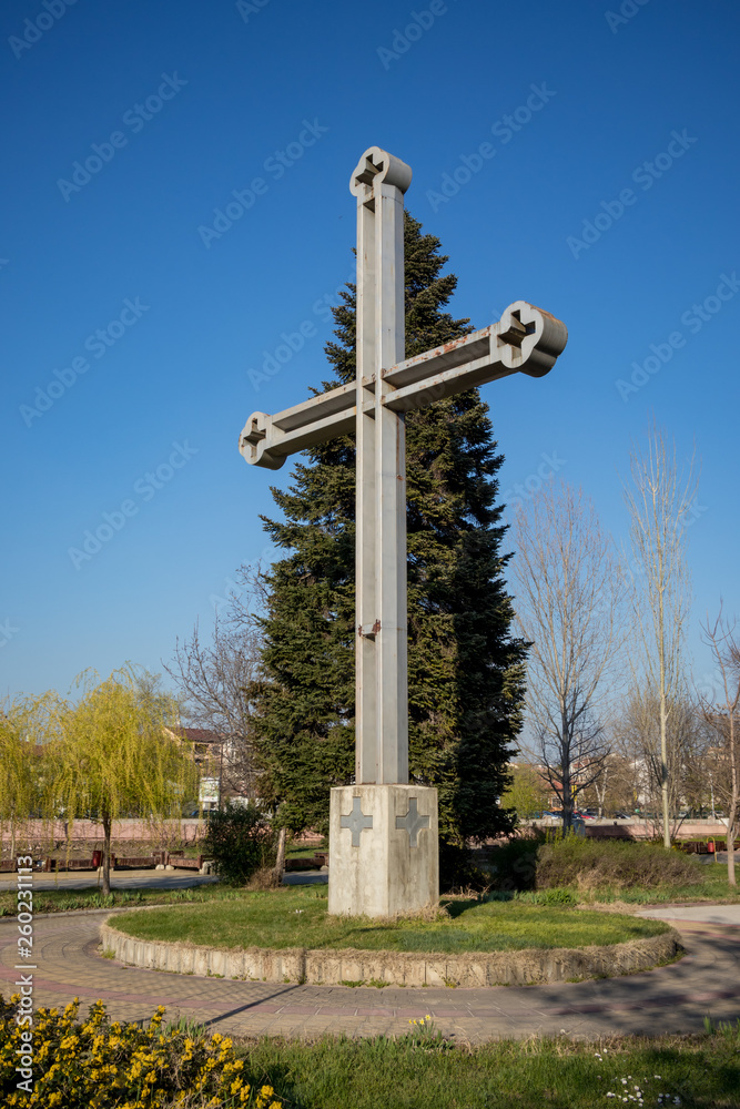 The big metallic Christian cross built on the Western side of island public park called Freedom in Pazardzhik, Bulgaria. Clear sky sunny early spring day. Leafless poplar trees in the background