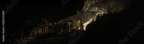 wide angle panoramic view showing the opening of a cave, Thum Lod cave, Bang Ma Pha, in Northern Thailand. Touristed cave with stalagmites and stalactites and a river running thru it. photo