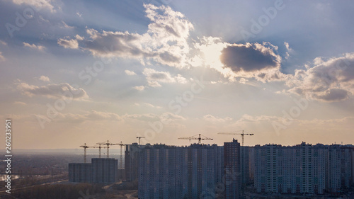 City landscape with new houses under construction on a background of cloudy sky with sunnlight. Aerial view of the drone.