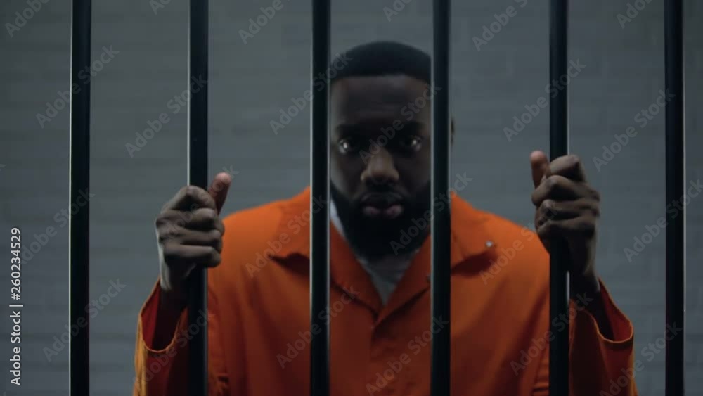 African-american male prisoner holding bars and looking to camera, imprisonment
