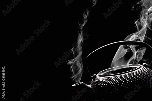 Antique rustic teapot on black background. Steaming tea pot. Cooking concept.