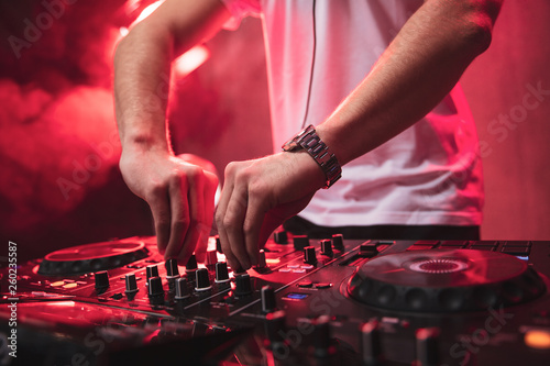 Dj mixing at party festival with red light and smoke in background - Summer nightlife view of disco club inside. Focus on hands photo