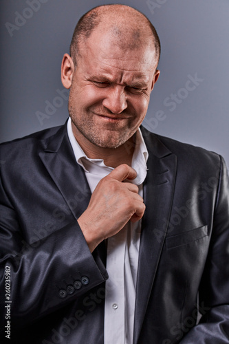 Unhappy stressed bald angry business man pulling the shirt collar with very bad emotions in office suit on grey studio background. Closeup