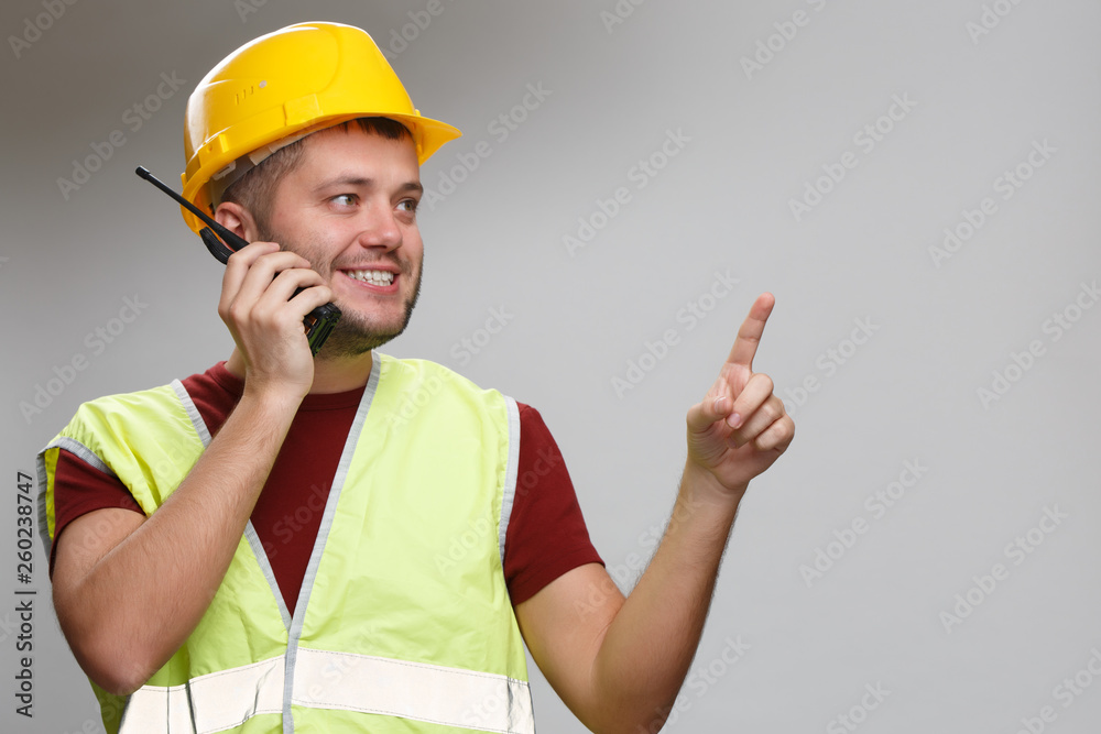 Photo of happy foreman in yellow helmet talking on walkie-talkie pointing his finger up in studio. Photo of happy foreman in yellow helmet talking on walkie-talkie pointing his finger up in studio.