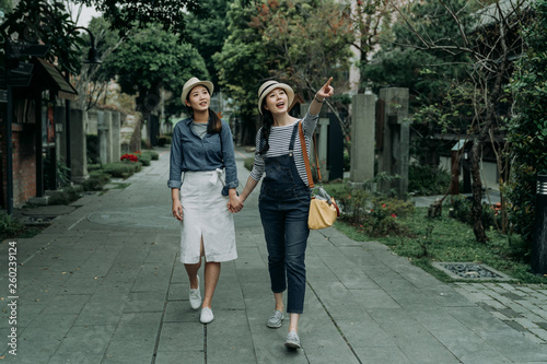 full length two women tourists talking going sightseeing in osaka japan travel. Happy girl friends travelers pointing up to blue sky showing sharing amazing view walking in pathway by japanese house © PR Image Factory