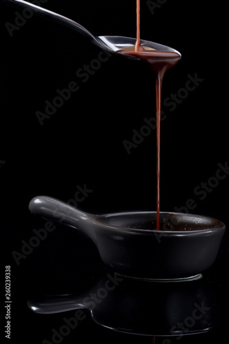 Melted milky brown chocolate pouring from a spoon, isolated on black