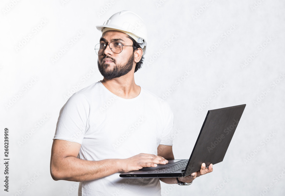 Young builder engineer in glasses and a white safety helmet, stands with an open laptop. Young builder engineer in glasses and a white safety helmet, stands with an open laptop.