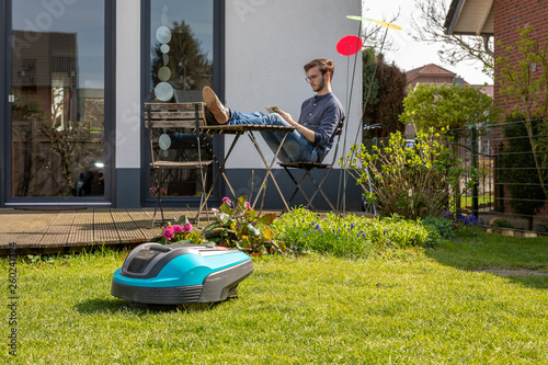 Mähroboter im Hintergrund Mann mit Buch