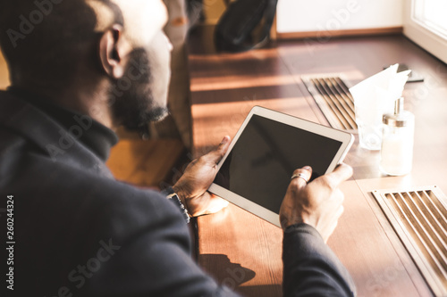 Young handsome dark-skinned businessman with tablet in cafe.