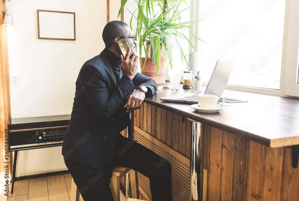 Young handsome dark-skinned businessman in a cafe talking on a cell phone with a cup of tea. Young handsome dark-skinned businessman in a cafe talking on a cell phone with a cup of tea.